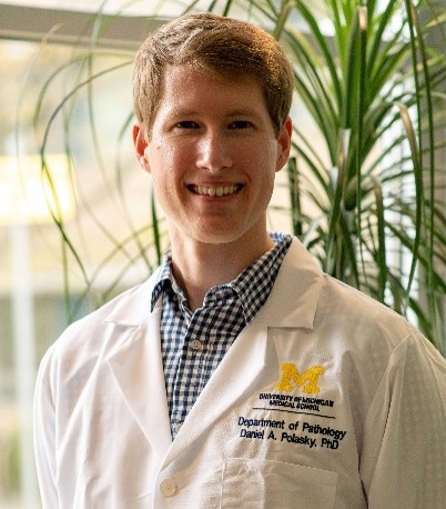 Dr. Daniel A. Polasky in a University of Michigan Medical School white coat embroidered "Department of Pathology", standing in front of green foliage.