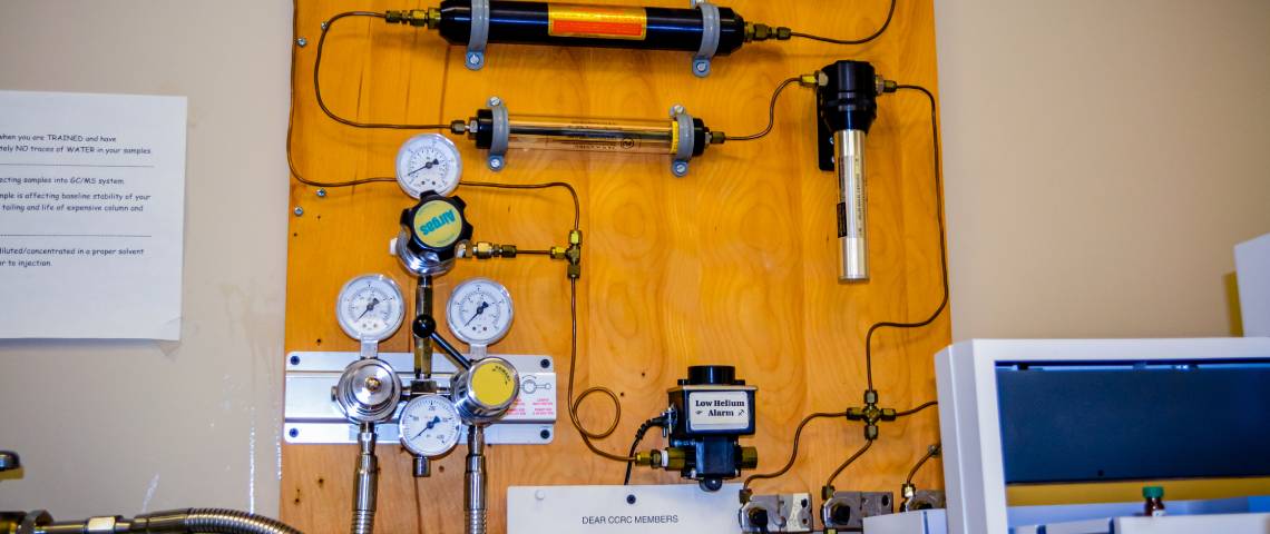 Gas regulators and a helium supply manifold mounted on a board beside a GC-MS instrument at the CCRC.