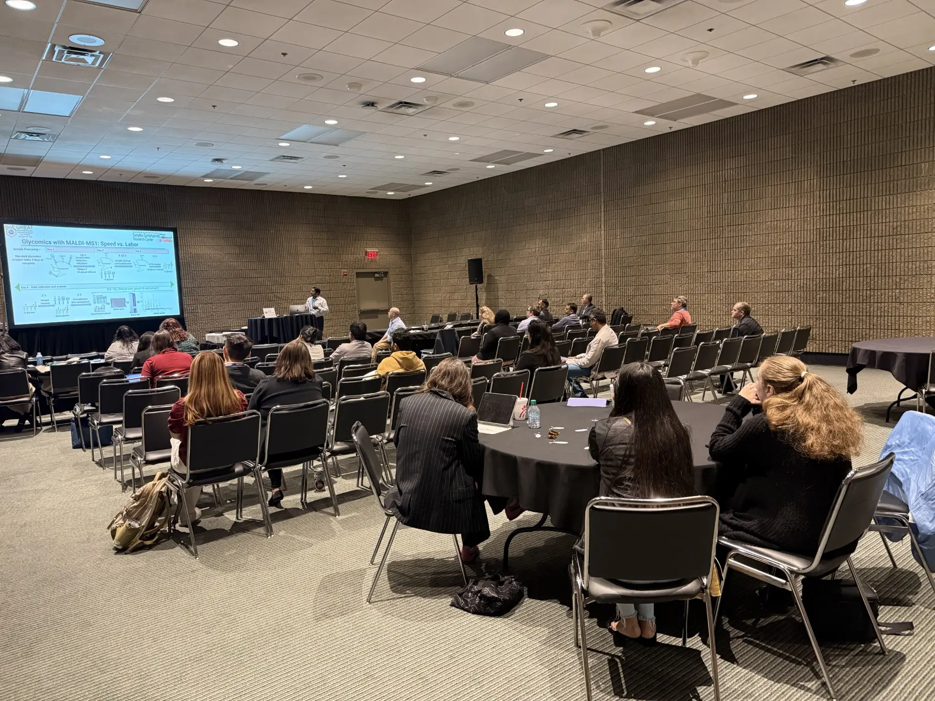 A seated audience watching a talk on glycomics with MALDI-MS.